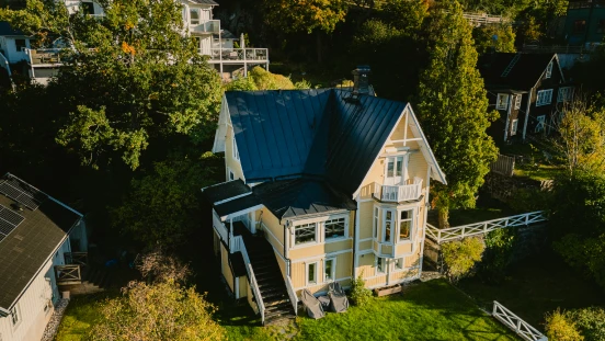 View over a yellow house with black roof surrounded by nature.
