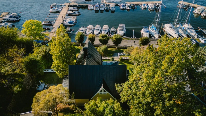 Overhead view of a villa in a forest area by the sea with boats in the harbor.